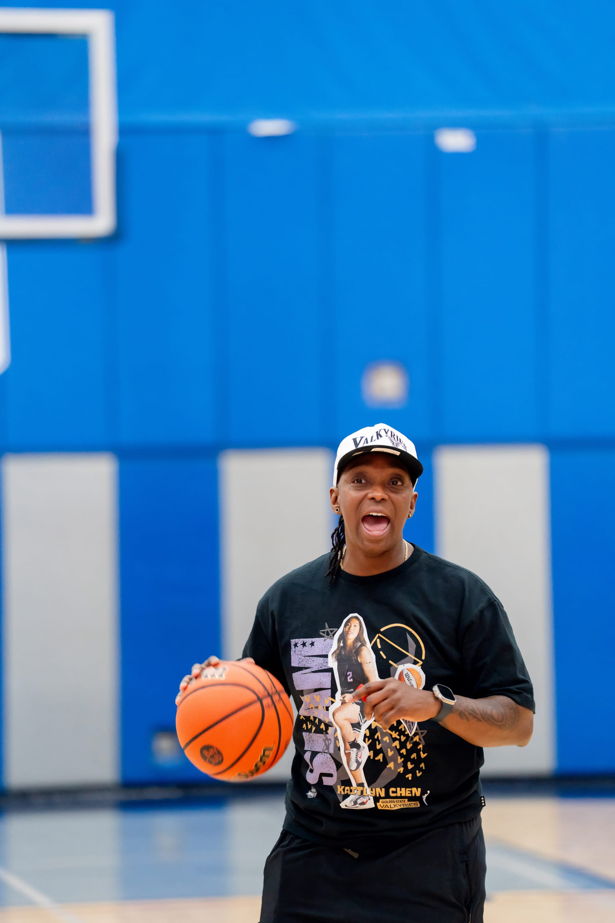Coach Tam McDonald in the gym, Valkyries cap, holding a basketball